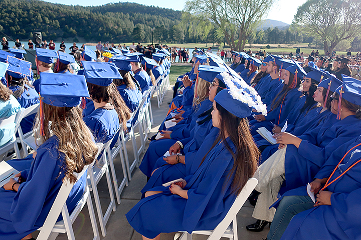 Rows of seated graduates in folding chairs outdoors.